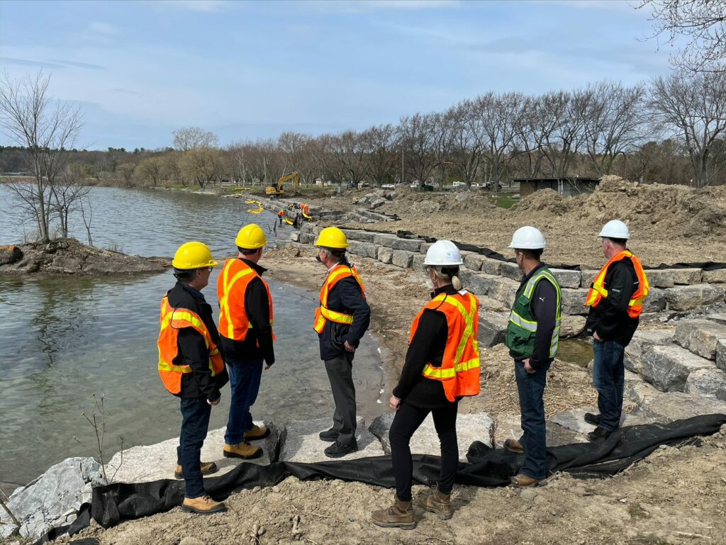 Various individuals in safety vest and hard hats overlooking body of water at Brown's Bay